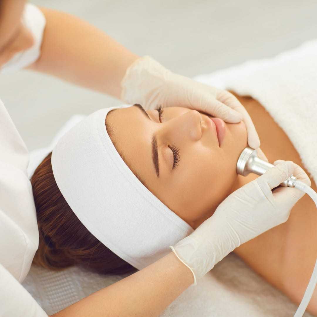 Woman receiving a facial treatment with a handheld device in a spa setting.
