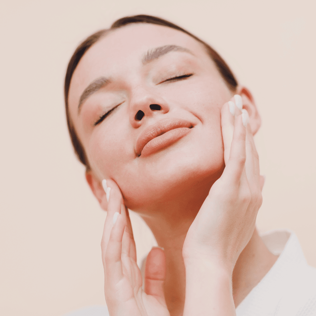 A woman gently touches her face, eyes closed, expressing skincare satisfaction.