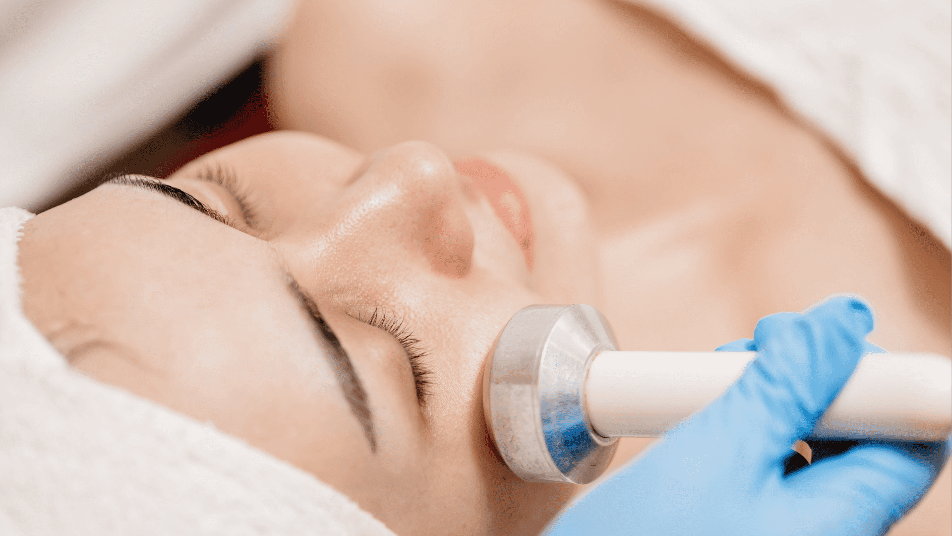 Skincare specialist using a device for a facial treatment on a relaxed woman in a spa.