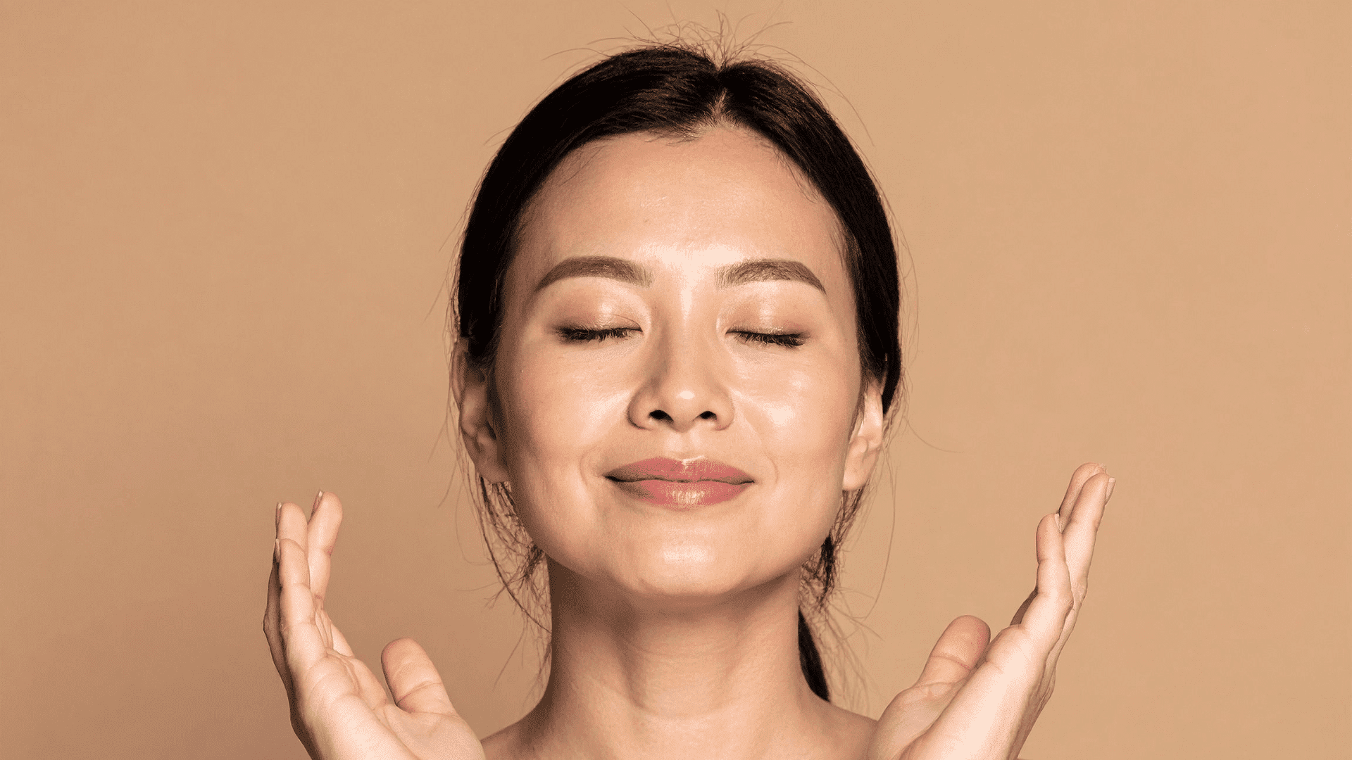 Smiling person with closed eyes, serene expression against a beige background.