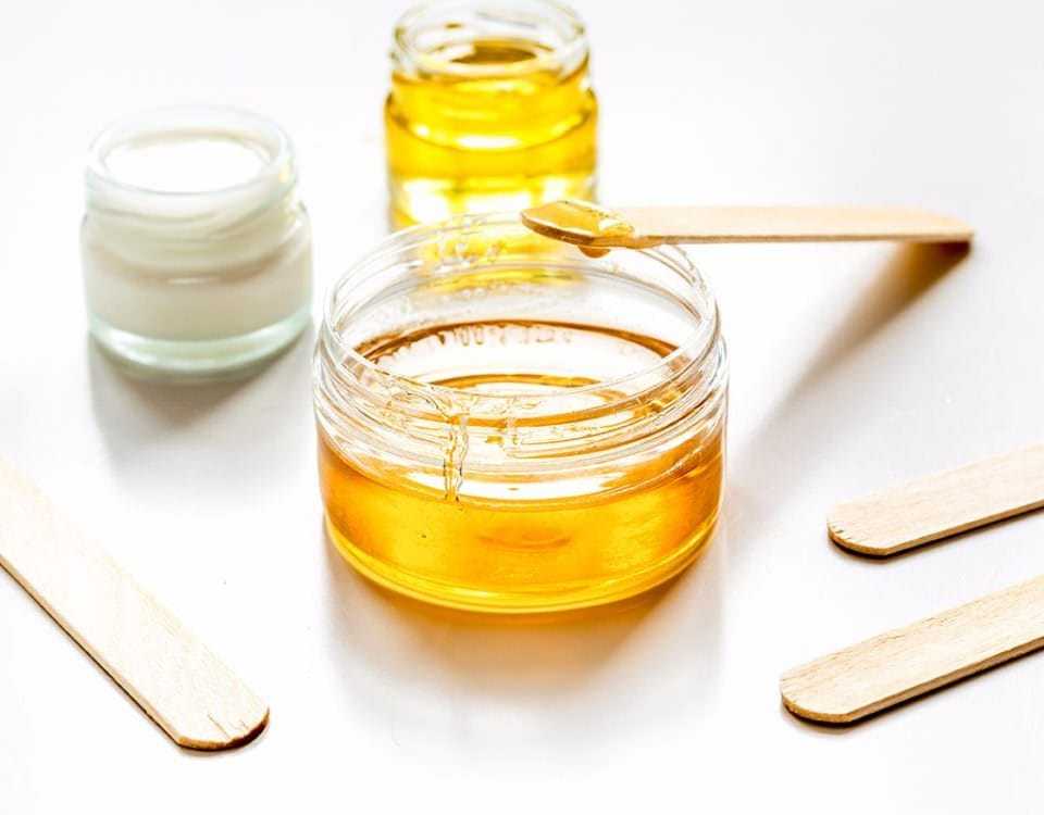 Jars of honey and cream with wooden spatulas on a white surface.