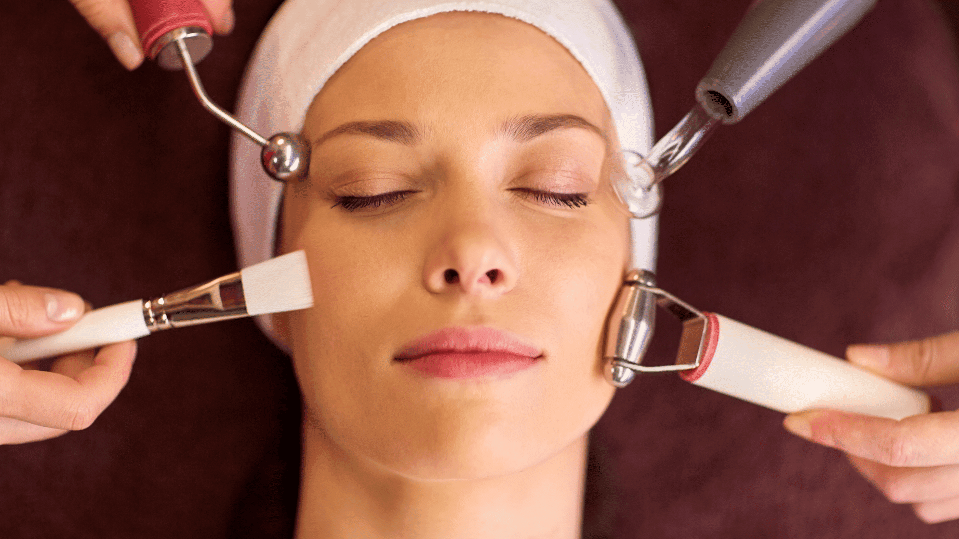 Woman receiving a multi-step facial treatment with various skincare tools at a spa.