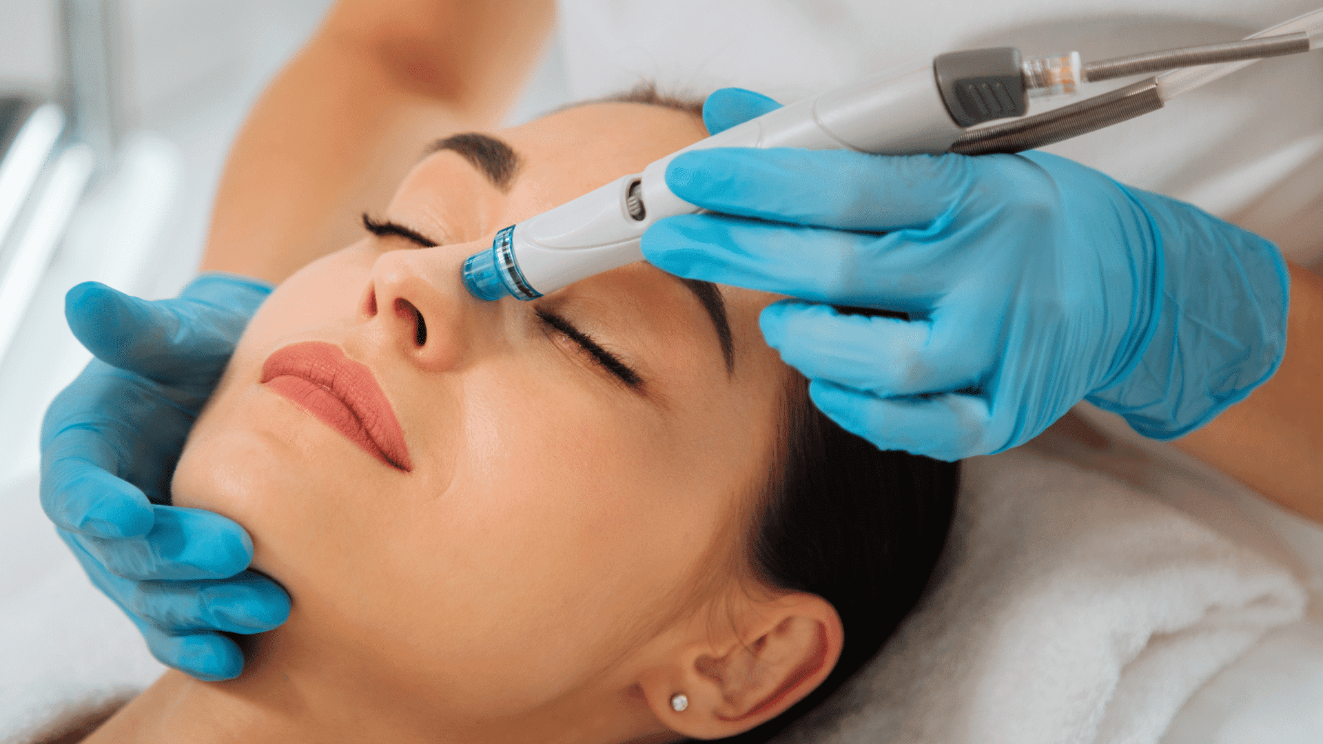 A beautician performs a facial treatment with a hydrodermabrasion device on a relaxed woman.